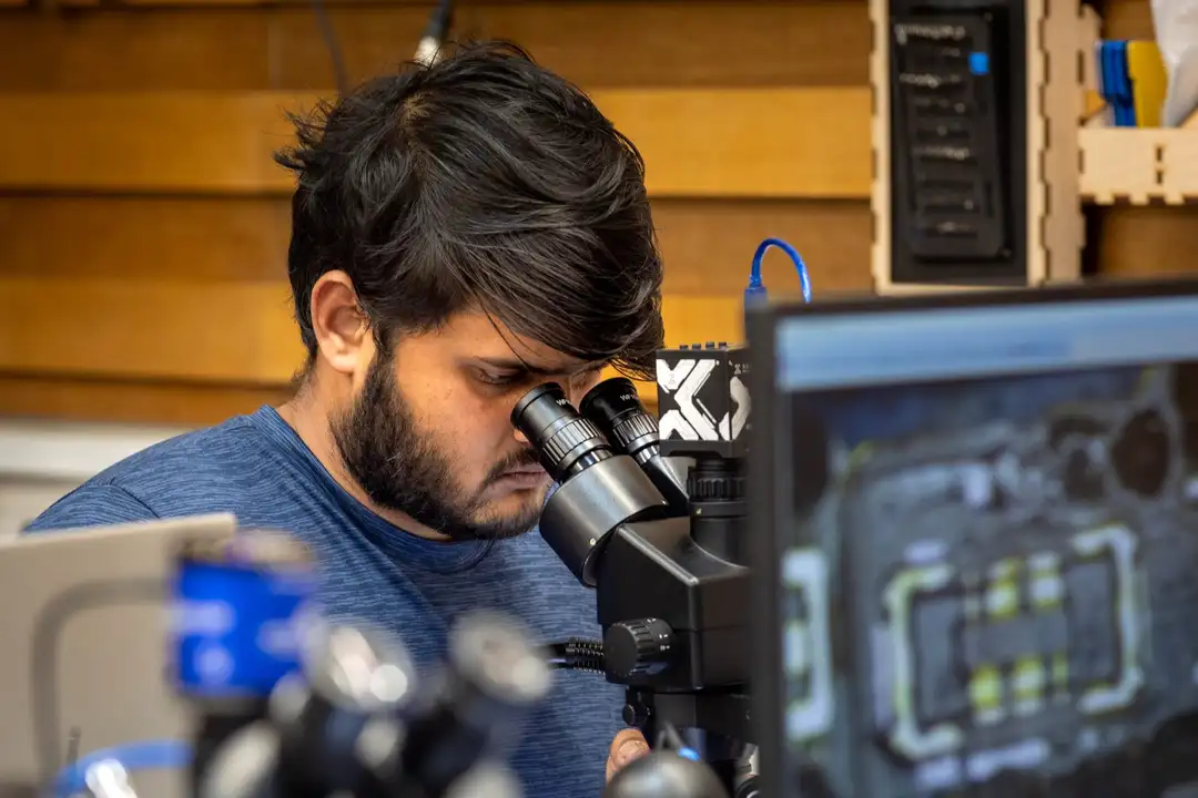 A student inspecting a logic board through a microscope