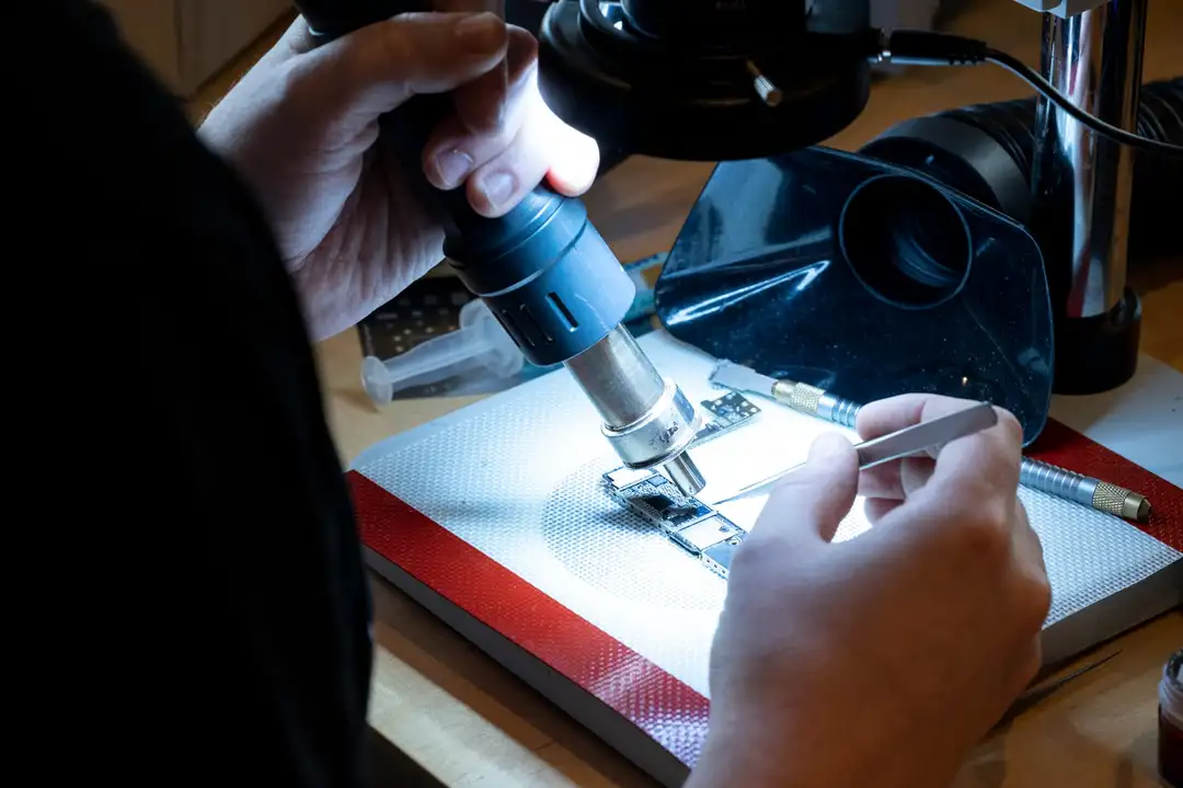 Hands working on a circuit board under a microscope